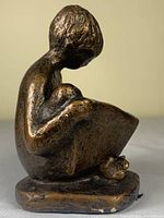 Front side view of bronze-like resin sculpture of boy reading book. Shows seated position with legs crossed and book held in lap.