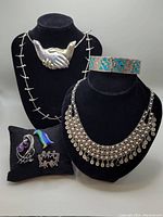Various necklaces displayed on busts and brooches on a cushion, alongside vintage silver and turquoise cuff bracelet.
