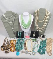 Front view of assorted vintage costume jewelry lot showing necklaces on busts and laid out beaded necklaces, bracelets, earrings, and brooches arranged in front