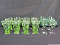 Eight green uranium glasses arranged in two groups on black background: four conical parfait glasses at left and four stemmed sherry glasses at right.
