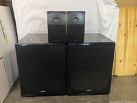 Front view of two large floor speakers and two smaller bookshelf speakers stacked
