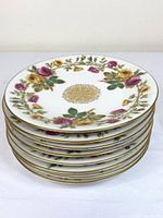 Stacked view of 8 Limoges luncheon plates decorated with hand painted pink and yellow roses and green leaves with gold rim and center medallion.