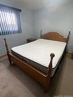 Full view of the assembled oak 4 post queen bed with white quilted mattress in bedroom.