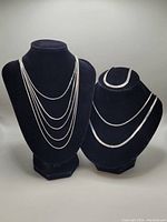 Photo showing multiple silver chain necklaces displayed on necklace busts to illustrate length and style.