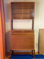 Full front view of teak hutch showing upper glass display case, two drawers and lower woven door cabinet