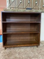 Front view of wooden bookcase showing three shelves and brown wood finish.
