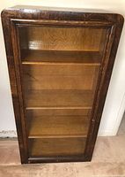 Front view of wooden bookcase with glass door showing three interior shelves.