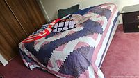 King sized quilt on bed showing purple, pink, and white geometric pattern.