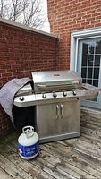 Full view of Char-Broil stainless steel commercial propane BBQ grill on patio with one propane tank on the ground nearby.