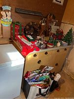 Wide view of assorted holiday decorations on a cabinet with wreath, ceramic tree, stockings, candles, and gift wrap bags below