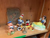 Photo showing full collection on wood shelf including Snow White music box figurine, Donald Duck, Mickey Mouse, Piglet, Winnie the Pooh, and antique Pinocchio book in background.
