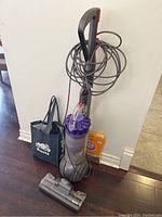 Full front view of Dyson DC42 Ball vacuum with cord wrapped around the handle, motorized cleaner head on floor, and accessories bag beside it.