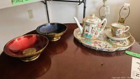 All items grouped on table: two enamel bowls on left and porcelain tea set on right