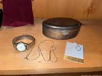 Wristwatch, gold chain, 10K gold hoop earring, and silver plate lined trinket box displayed on wooden shelf.