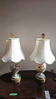 Two matching vintage lamps displayed together with fabric scalloped shades and floral painter glass bases.