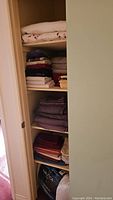 Photo of linen closet shelves showing neatly folded towels and sheets in various colors including white, burgundy, purple, cream