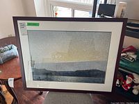 Framed artwork showing a landscape scene under a cloudy sky in muted blue and yellow tones, housed in a dark wooden frame with white and blue double mats. Overall size 27.5x43.5 inches.