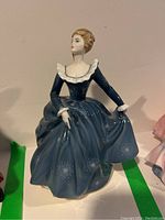 Front view of Royal Doulton porcelain figurine, showing woman in dark blue dress with white collar and cuff details, holding skirt sides.