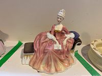 Front view of Royal Doulton figurine 'Reverie' seated on chaise lounge in pink dress.