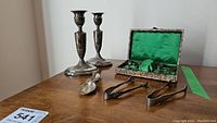 Overview of two candlesticks, one loose spoon, two tongs, and fitted case