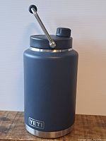 Large matte black Yeti thermos with metal handle on rustic wood surface against white background