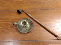 Brass candle holder and candle snuffer placed on a wooden surface showing the entire items.