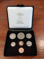 Black display case open showing seven Canadian coins neatly arranged in custom slots, white lid interior labeled with Royal Canadian Mint branding.
