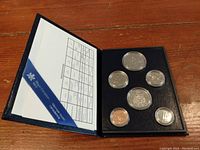Open blue display folder showing six Canadian coins in protective capsules with coin specification card on left side.
