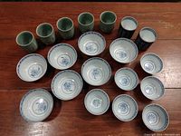 Full view of the twenty ceramic pieces on wooden surface showing both tea cups and bowls.