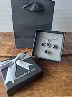 Packaging including gift bag and black box with "Best wishes to you" ribbon, containing the jewelry set