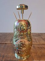 Front view showing colorful embossed design and toothpicks inside dispenser with push button top.