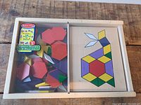 Top view of wooden toy pattern blocks inside a wooden box with geometric colorful shapes and a pattern board showing a rabbit design.