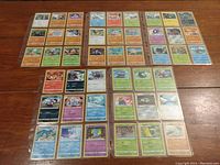 45 Pokemon trading cards laid out in sleeves on a wooden surface, showing a variety of Pokemon species and card types.
