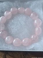 Rose quartz bracelet with smooth oval and round large pink beads, placed on a soft fabric background.