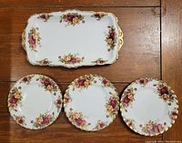 Top-down view of the sandwich tray and three side plates arranged on a wooden surface, showing the Old Country Roses floral and gold trim design.