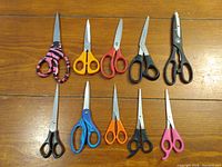 Photo showing ten pairs of scissors with diverse handle colors and sizes laid out on a wooden surface.