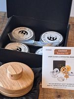 Open box showing wooden smoker with lid, four metal containers labeled Apple Wood Chips, metal mesh brush, and user guide