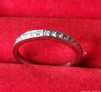 Close-up image of the silver-toned ring with a row of small white stones set around the band, showing the ring from the side in a red ring box.