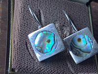 Close-up front view of one sterling silver earring showing a circular abalone shell inset in a square setting.