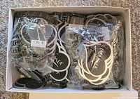 Box filled with packaged and loose black stretch bracelets with 'OK' silver-tone tags inside a white box