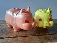 Photo showing pink and yellow vintage plastic piggy banks from front angle, marker marks visible on top.