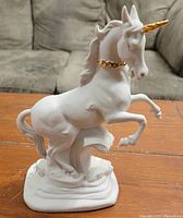 Front view of the white porcelain unicorn figurine with gold horn and collar on wooden table.