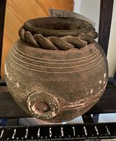 Front view of dark ceramic round pot displaying rope trim and side handle, scale ruler visible for size reference.