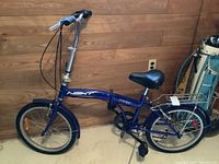 Side view of blue Next Stowaway folding bike showing frame, saddle, and handlebar details.