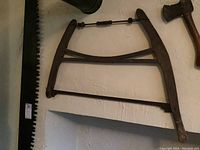 Photo of vintage wood handled bow saw lying flat on white surface, showing wooden frame, metal blade, and tensioning rod.