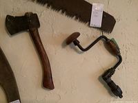 Vintage 12-inch hatchet and brace hand drill hanging on a wall, showing their overall condition and size comparison.