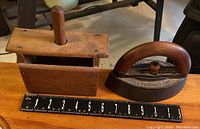 Top and side view of wooden butter stamp and cast iron sad iron next to a ruler for scale showing 9 inch length for butter stamp and 5 inch height for sad iron handle.
