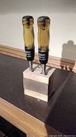 Photo showing three Stanley Professional wood chisels with amber handles inserted into a small butcher block wood holder on a table surface.
