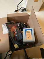 Photo showing a box containing the Motomaster power inverter in sealed package, digital timer in box, assorted wires and the MBK battery charger partially visible.