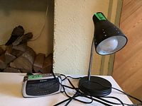 Photo showing both the black flexible neck desk lamp and the Emerson portable alarm clock radio placed on a white surface.